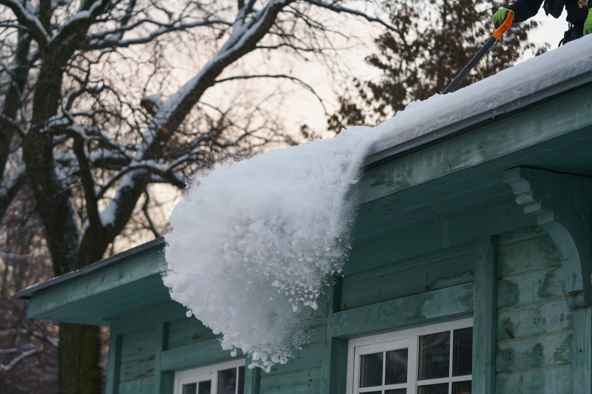 Ice dam prevention. Man holding shovel cleaning roof from snow, ice and icicles during wintertime
